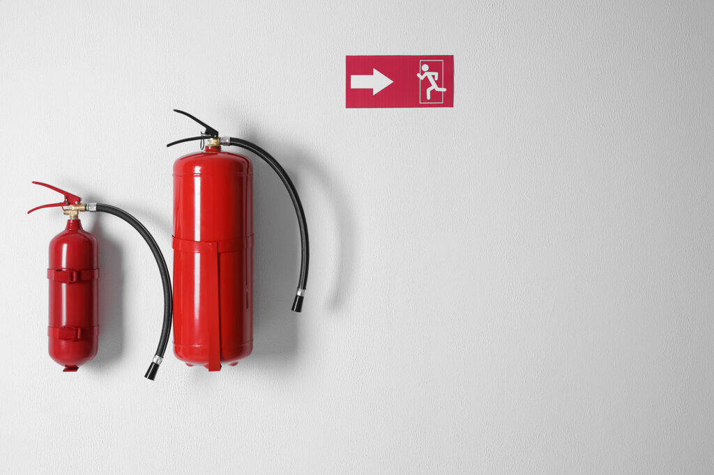 Two red fire extinguishers on a wall with an exit sign